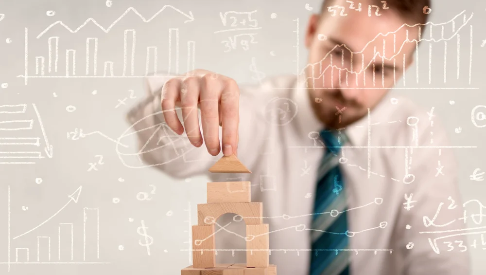 Young handsome businessman using wooden building blocks with white calculations scribbled around him